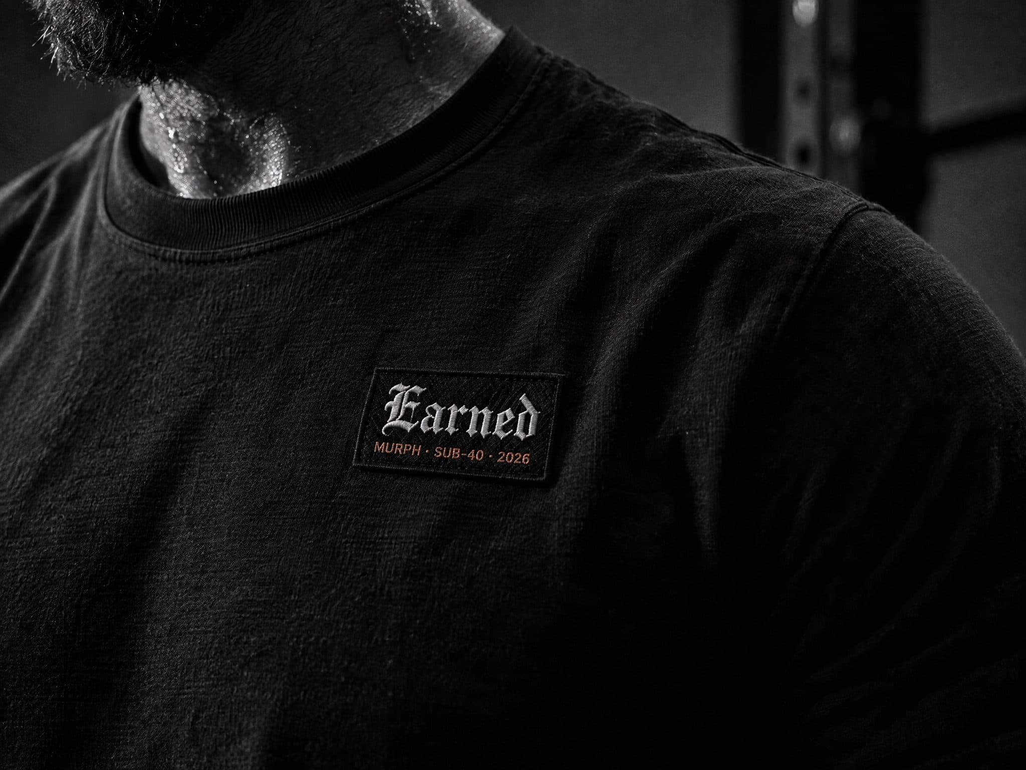 Black t-shirt with a small Earned patch reading Murph, sub-40, 2026