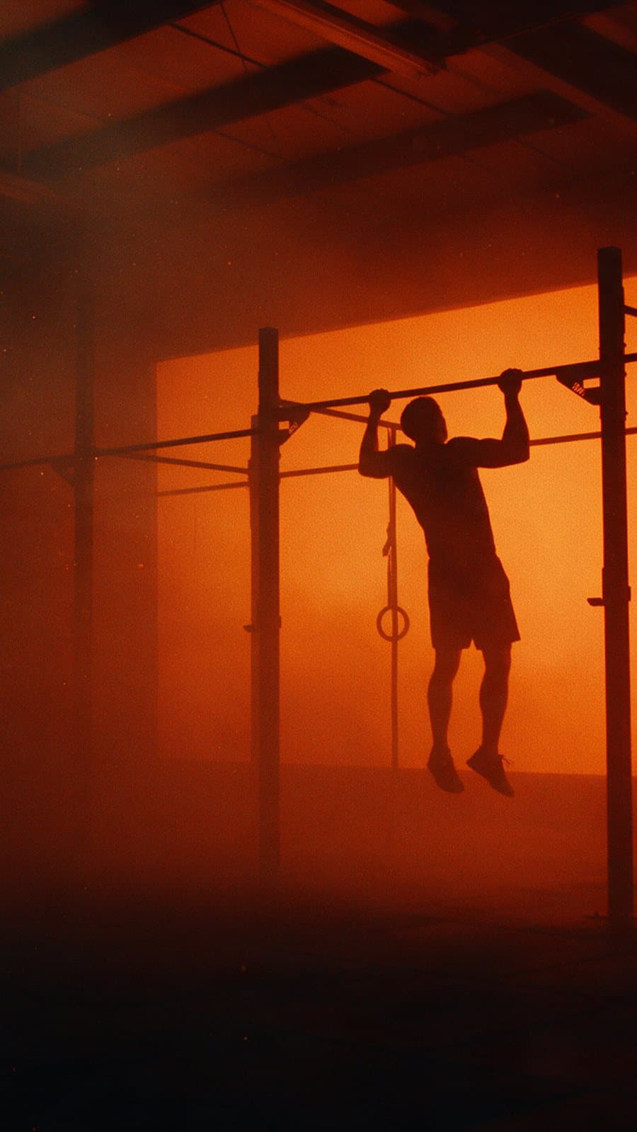 Athlete doing pull-ups on a steel rig, silhouetted against orange haze