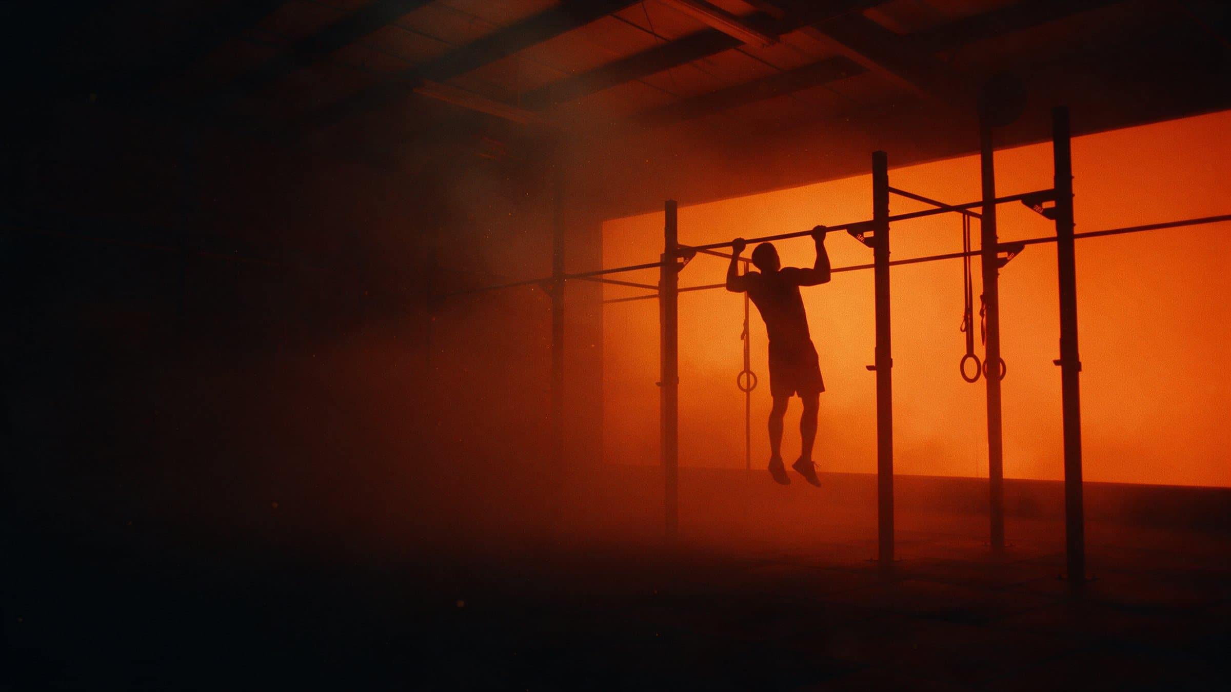 Athlete doing pull-ups on a steel rig, silhouetted against orange haze